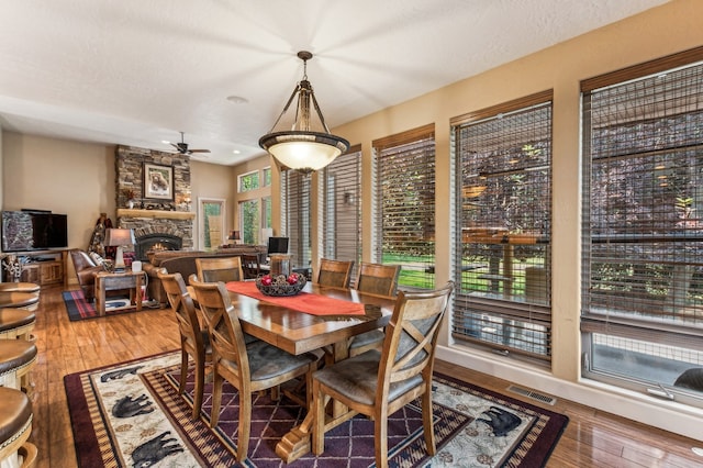 dining area with a stone fireplace, a textured ceiling, ceiling fan, and wood-type flooring