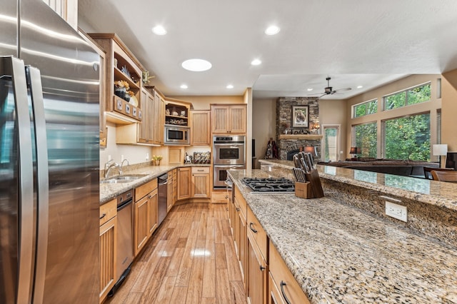 kitchen with appliances with stainless steel finishes, sink, light stone counters, light hardwood / wood-style floors, and ceiling fan