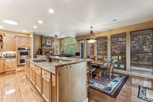 kitchen with decorative light fixtures, a kitchen island, appliances with stainless steel finishes, light hardwood / wood-style flooring, and stone countertops