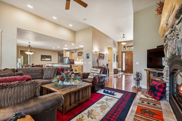 living room with a stone fireplace, ceiling fan, and wood-type flooring