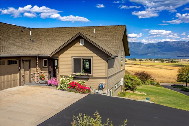 view of front of property with driveway, stone siding, a shingled roof, an attached garage, and a mountain view