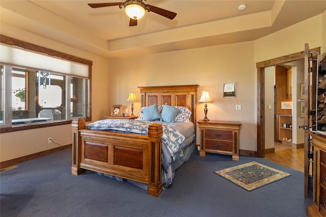 carpeted bedroom with baseboards, a tray ceiling, and ceiling fan