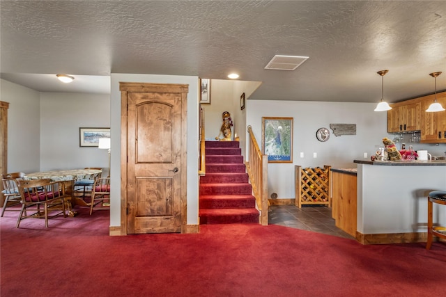 kitchen with visible vents, baseboards, dark carpet, brown cabinetry, and decorative light fixtures