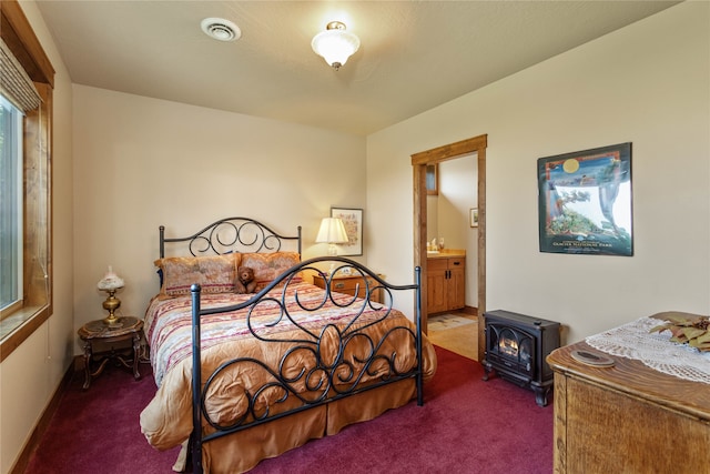 bedroom featuring a wood stove, carpet, and ensuite bathroom