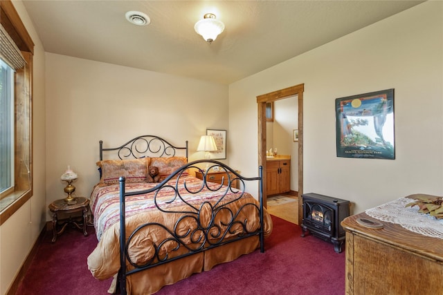 carpeted bedroom featuring connected bathroom, a wood stove, and visible vents