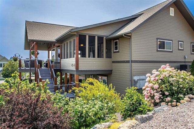 view of property exterior featuring stairway, a shingled roof, and a sunroom