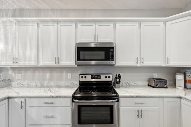 kitchen with a toaster, appliances with stainless steel finishes, white cabinetry, and light stone countertops