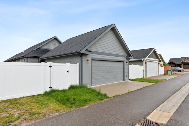 view of home's exterior featuring a garage, a gate, fence, and roof with shingles