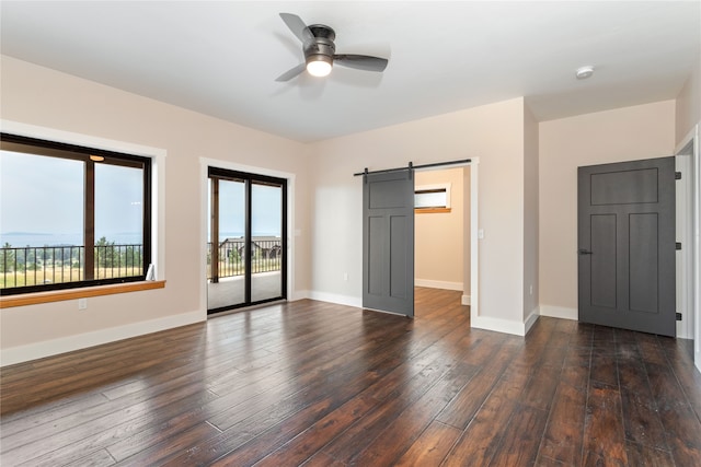 unfurnished bedroom with a barn door, dark hardwood / wood-style floors, ceiling fan, and access to exterior