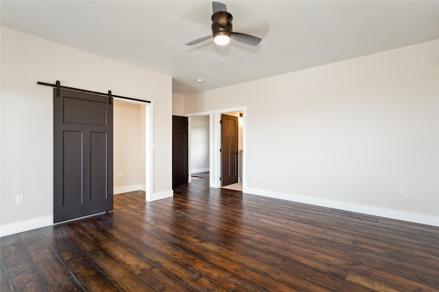 unfurnished bedroom featuring a barn door, dark hardwood / wood-style flooring, and ceiling fan