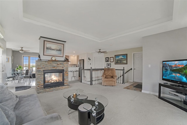 living area featuring baseboards, a raised ceiling, light colored carpet, ceiling fan, and a fireplace