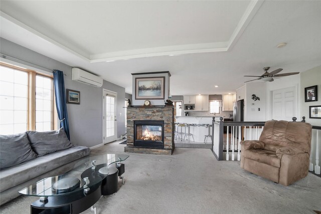 living area with a tray ceiling, a wall unit AC, a fireplace, and light carpet