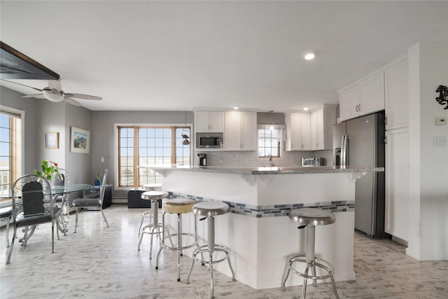 kitchen featuring stainless steel appliances, a wealth of natural light, decorative backsplash, white cabinets, and a kitchen breakfast bar