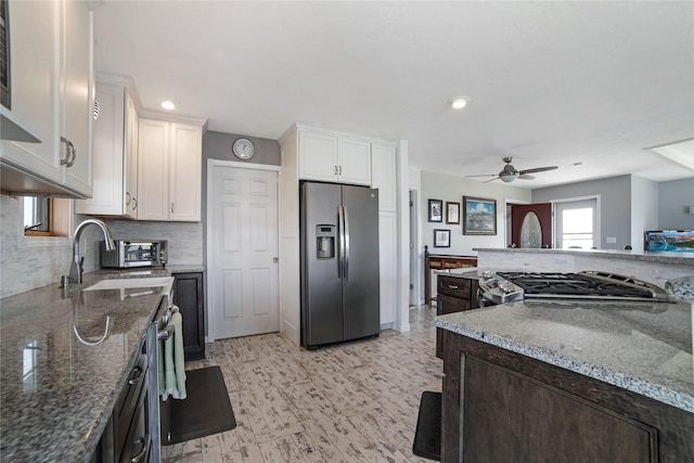 kitchen featuring stainless steel fridge, decorative backsplash, dark stone counters, stove, and white cabinetry