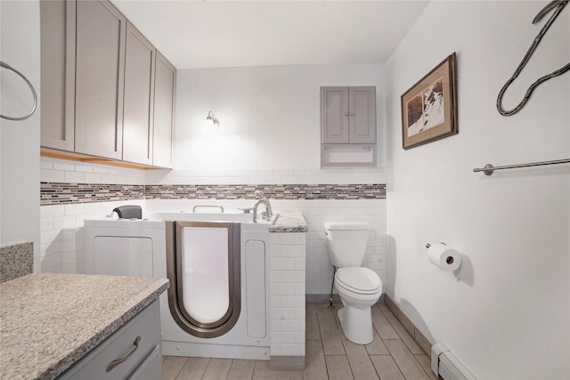 bathroom featuring toilet, a baseboard radiator, wood finished floors, independent washer and dryer, and tile walls