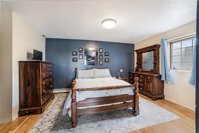 bedroom with a baseboard heating unit, baseboards, and light wood-style floors