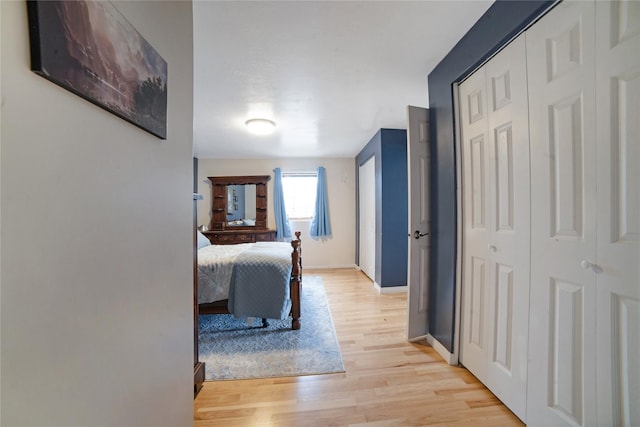 bedroom with a closet, light wood-type flooring, and baseboards