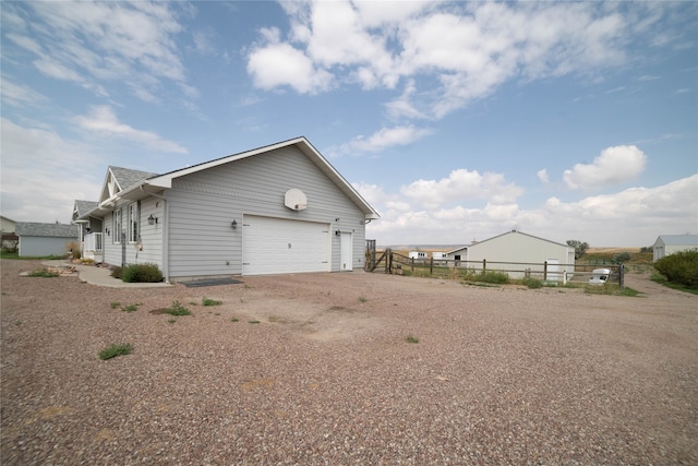 view of side of property featuring dirt driveway, fence, and a garage