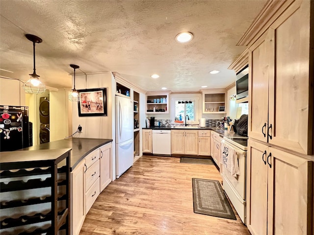 kitchen with sink, a textured ceiling, stacked washer / dryer, white appliances, and hanging light fixtures