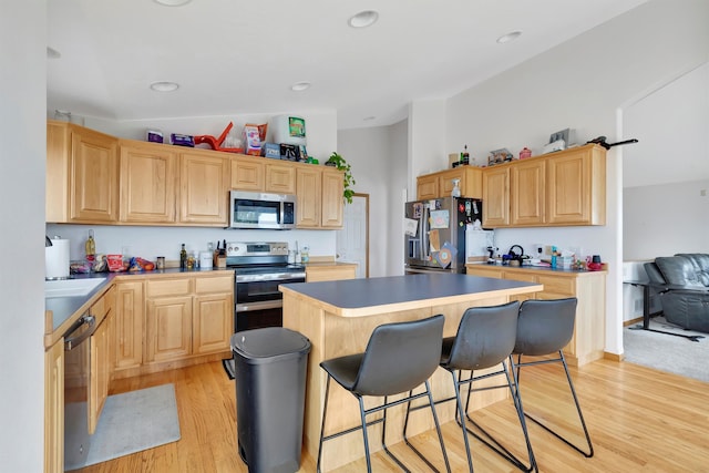 kitchen featuring appliances with stainless steel finishes, light hardwood / wood-style floors, a kitchen breakfast bar, light brown cabinetry, and a center island