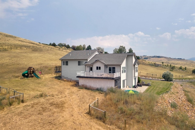 rear view of house featuring a wooden deck, a playground, and a rural view