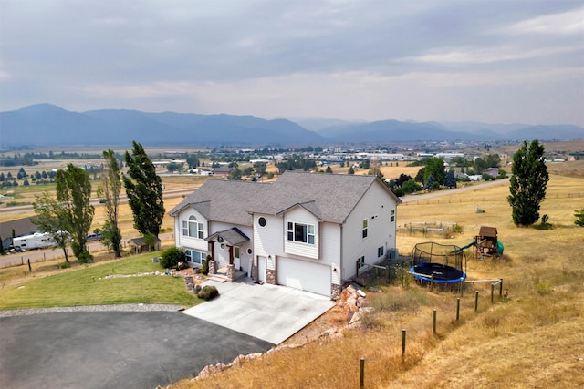 view of front facade featuring a front lawn, a mountain view, a garage, and a trampoline