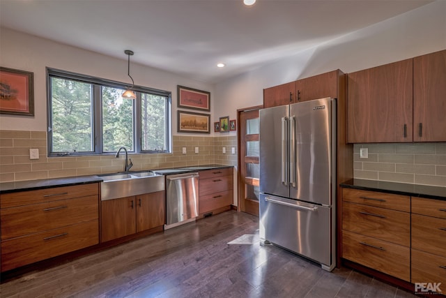 kitchen featuring appliances with stainless steel finishes, sink, backsplash, decorative light fixtures, and dark wood-type flooring