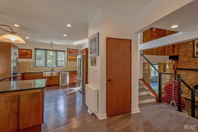 kitchen with appliances with stainless steel finishes, sink, pendant lighting, backsplash, and dark wood-type flooring