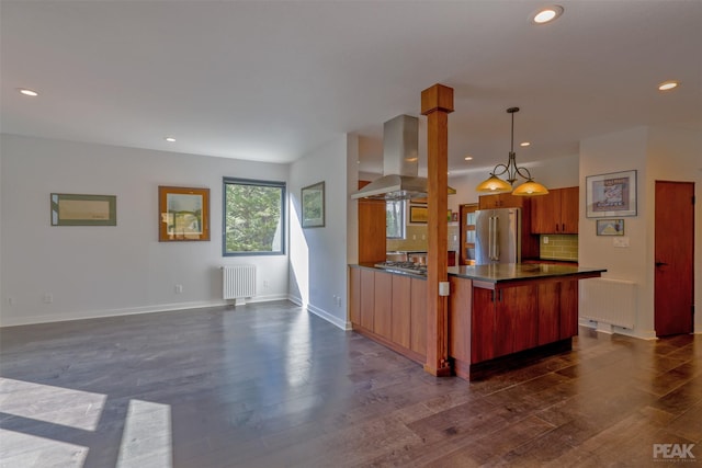 kitchen with hanging light fixtures, radiator heating unit, wall chimney exhaust hood, and appliances with stainless steel finishes