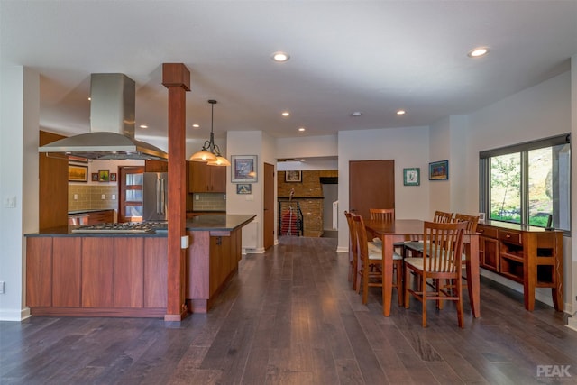 kitchen with appliances with stainless steel finishes, island range hood, decorative light fixtures, tasteful backsplash, and kitchen peninsula