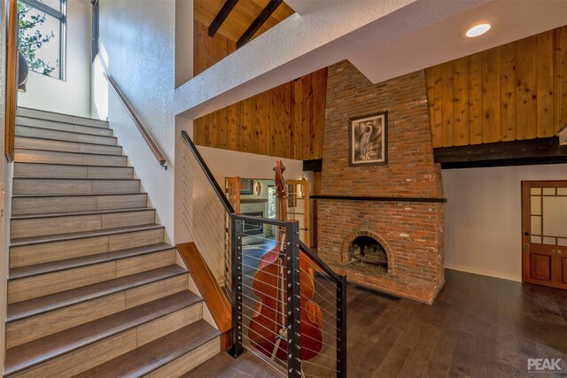 stairway featuring brick wall, beam ceiling, high vaulted ceiling, wood walls, and wood-type flooring