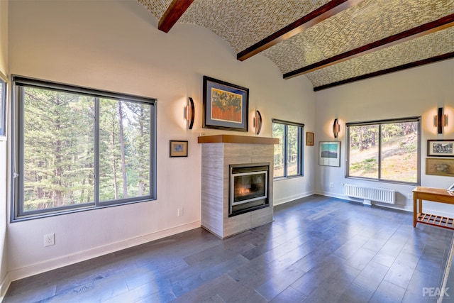 unfurnished living room featuring beamed ceiling, a wealth of natural light, a fireplace, and dark wood-type flooring