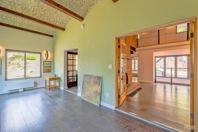 interior space featuring beamed ceiling, wood-type flooring, a wealth of natural light, and radiator heating unit