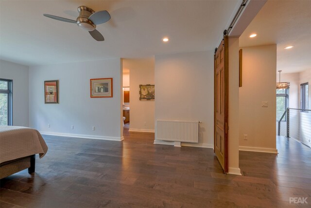 bedroom with radiator heating unit, dark wood-type flooring, ceiling fan, and a barn door