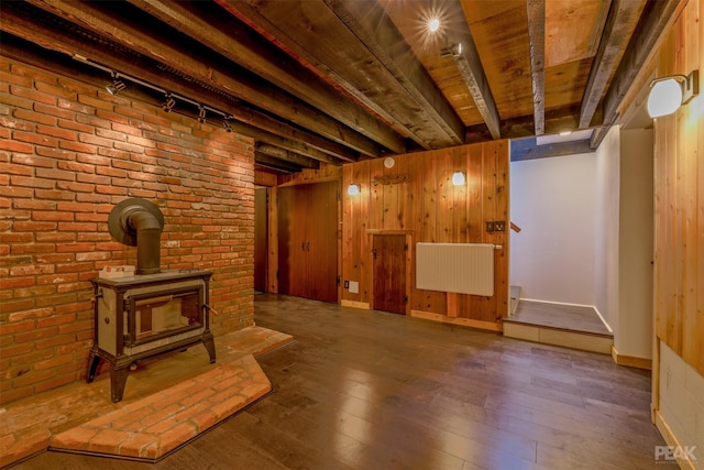 basement featuring wooden walls, a wood stove, dark hardwood / wood-style flooring, wood ceiling, and track lighting