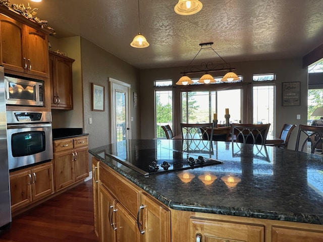 kitchen featuring appliances with stainless steel finishes, dark hardwood / wood-style flooring, a textured ceiling, decorative light fixtures, and dark stone countertops