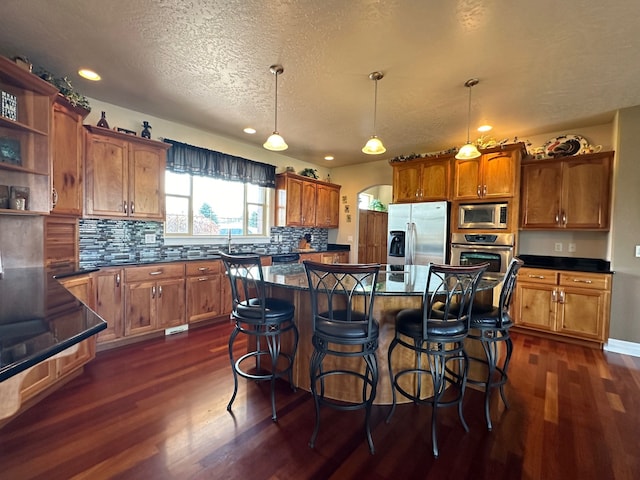 kitchen with a breakfast bar, a center island, dark hardwood / wood-style floors, appliances with stainless steel finishes, and decorative light fixtures