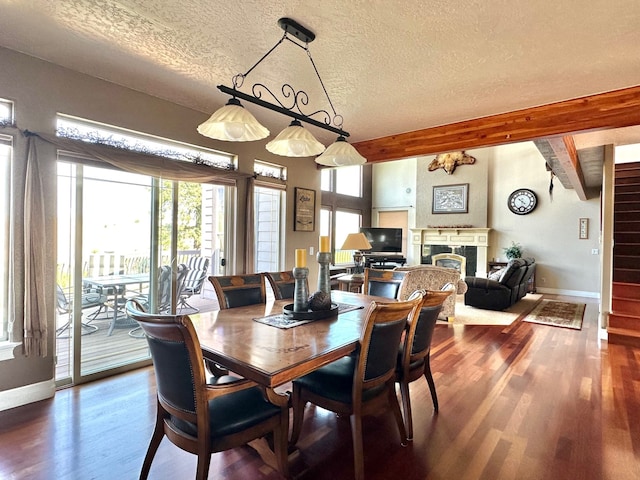 dining space with beamed ceiling, wood-type flooring, a textured ceiling, and a tile fireplace