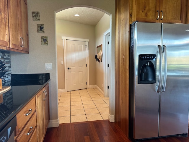 kitchen featuring brown cabinetry, arched walkways, dark countertops, baseboards, and stainless steel fridge