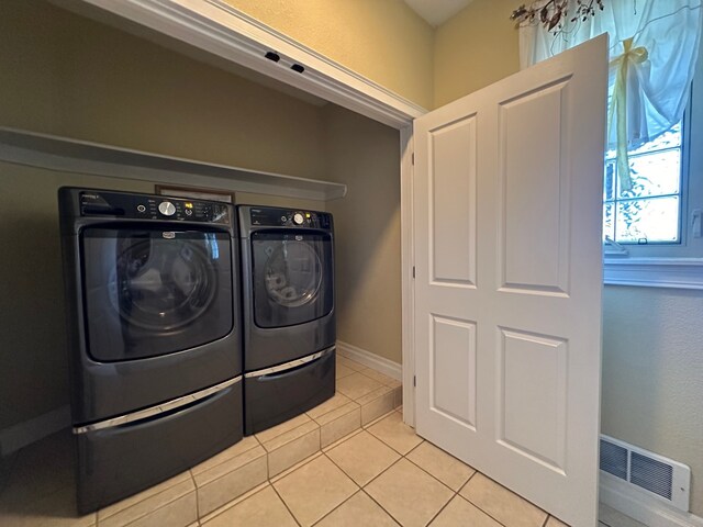 clothes washing area featuring laundry area, visible vents, light tile patterned flooring, washer and dryer, and baseboards