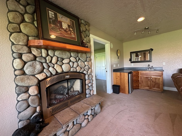 carpeted living room with a stone fireplace, a sink, a textured ceiling, and wet bar