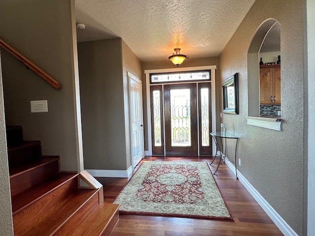 foyer with a textured wall, a textured ceiling, stairs, baseboards, and wood finished floors