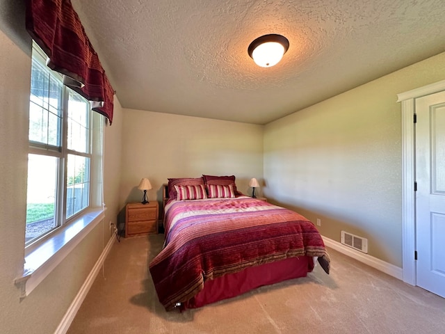 bedroom featuring carpet floors, a textured ceiling, visible vents, and multiple windows