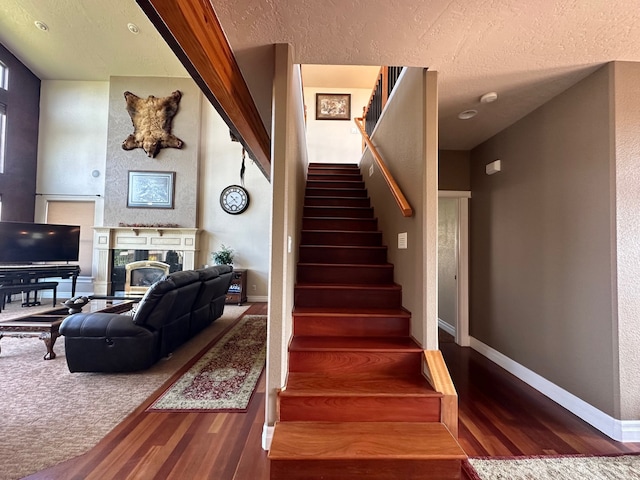 stairs with baseboards, a textured ceiling, a glass covered fireplace, and wood finished floors