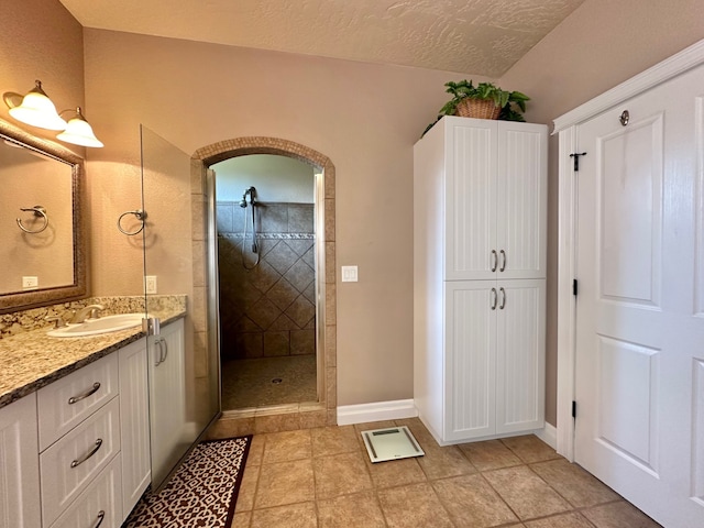 bathroom with vanity, a tile shower, lofted ceiling, and a textured ceiling