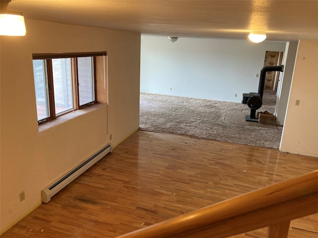 empty room featuring a wood stove, baseboard heating, and wood-type flooring