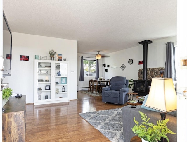 living room with a baseboard radiator, a wood stove, dark hardwood / wood-style flooring, ceiling fan, and a textured ceiling