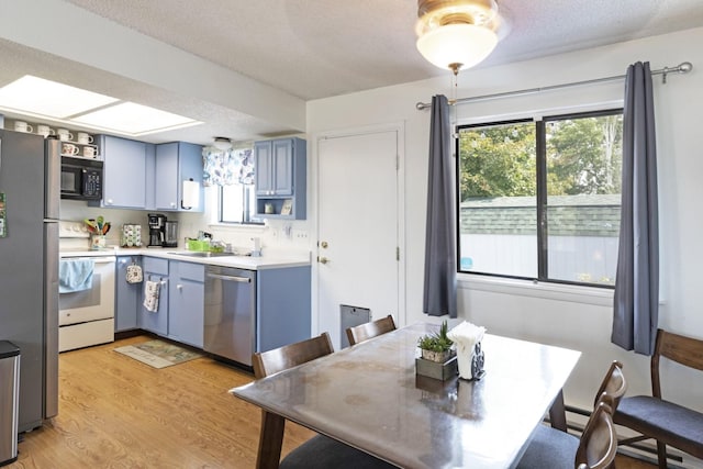 kitchen featuring appliances with stainless steel finishes, blue cabinets, a textured ceiling, and light wood-type flooring