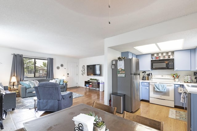 interior space featuring white range with electric stovetop, a skylight, stainless steel fridge, a textured ceiling, and light wood-type flooring