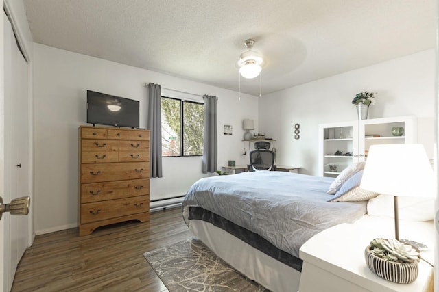 bedroom featuring a baseboard heating unit, ceiling fan, dark wood-type flooring, a textured ceiling, and a closet